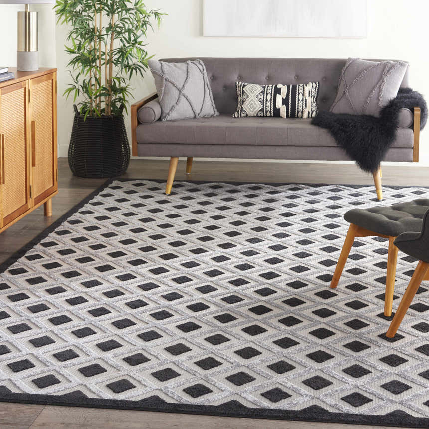 Living room scene with a Nourison Aloha Black White rug, gray sofa, wood cabinet, and potted plant.