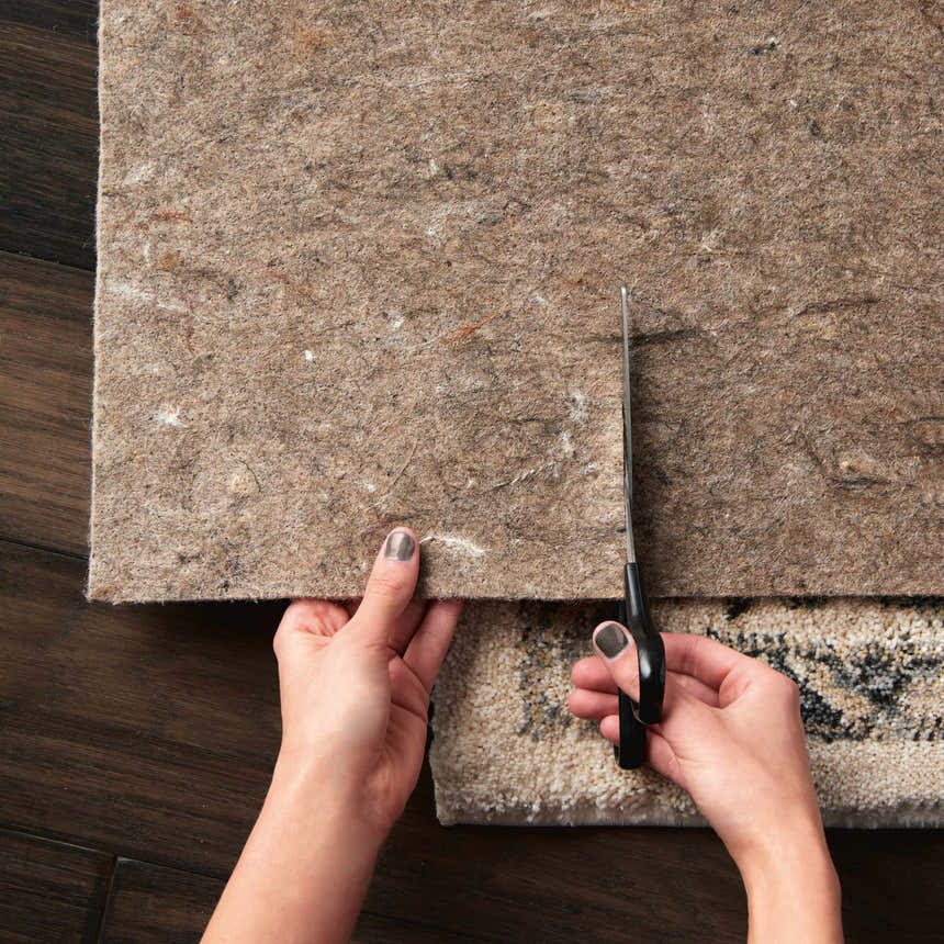 Cutting a Nourison Loc Non-slip Pad to fit a rug on a dark wood floor.