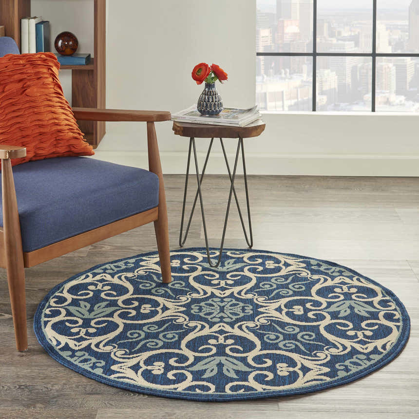 Living room scene with a round Nourison Caribbean Navy Contemporary Area Rug, blue chair, wood table, and city view.