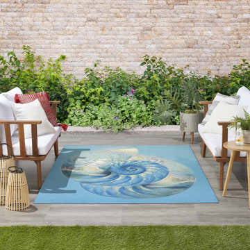 Coastal patio with white sofas and Nourison Color Splash Blue Ivory Area Rug featuring a nautilus shell design.