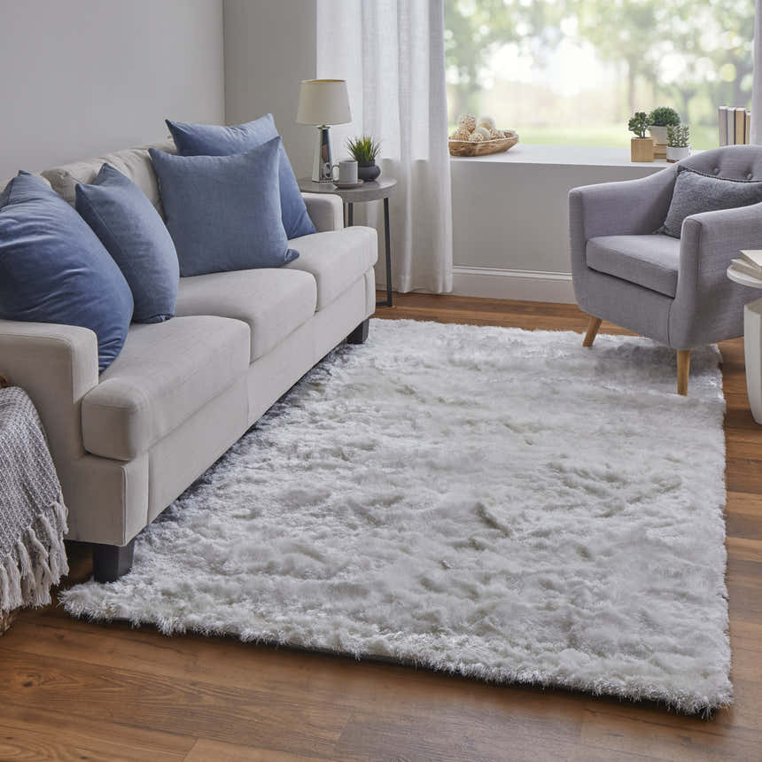 Living room scene with a Feizy Indochine Modern Solid White area rug, light sofa with blue pillows, and gray armchair. Roomscene-Rectangle