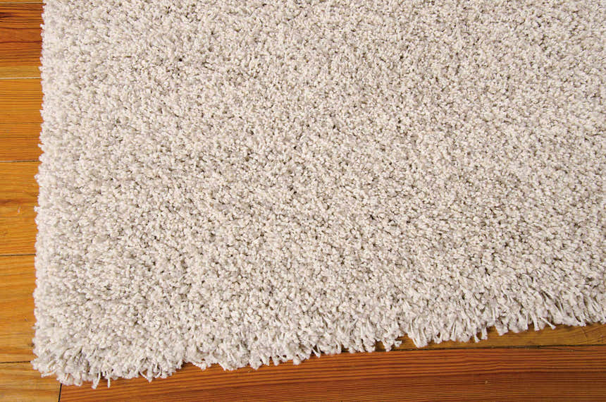 Close-up of the plush, beige Nourison Amore Bone Shag rug showing its soft texture and shaggy fringe detail on wood floor.