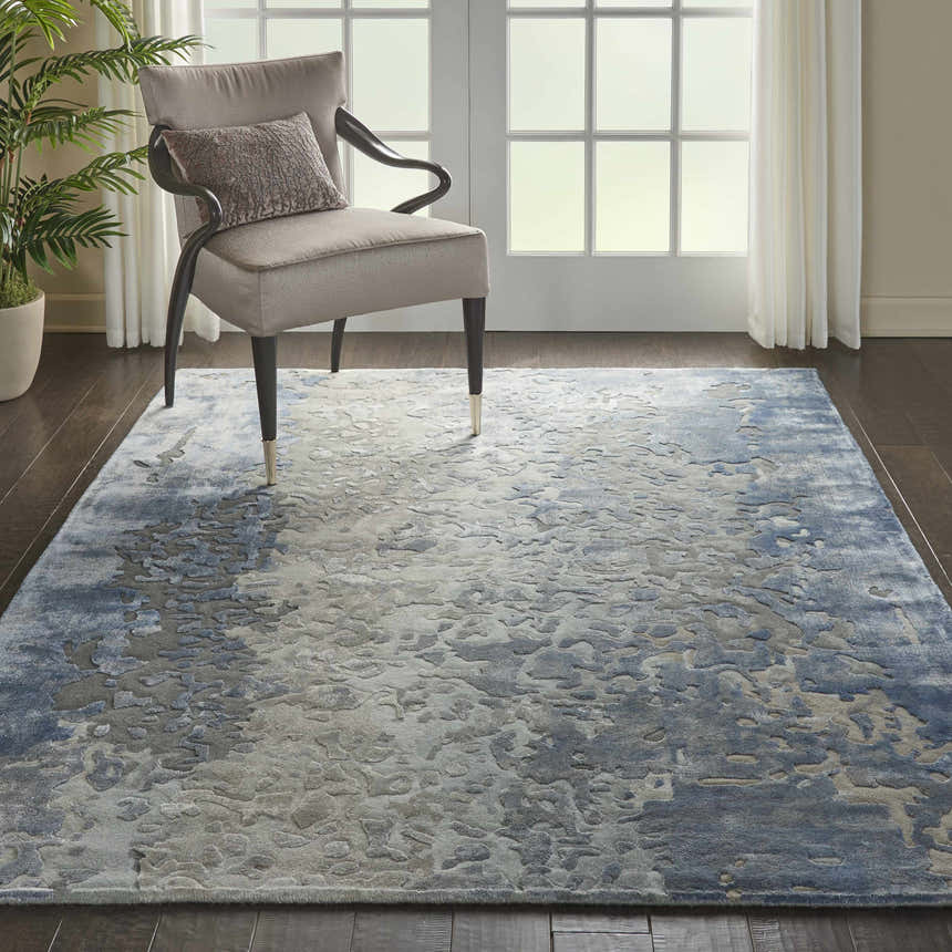 Living room scene with a Nourison Prismatic Denim rug, gray chair, dark wood floors, and natural light.