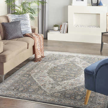 Living room scene with a Nourison Starry Nights Grey Blue vintage rug, tan sofa, fireplace, and blue accent chair.
