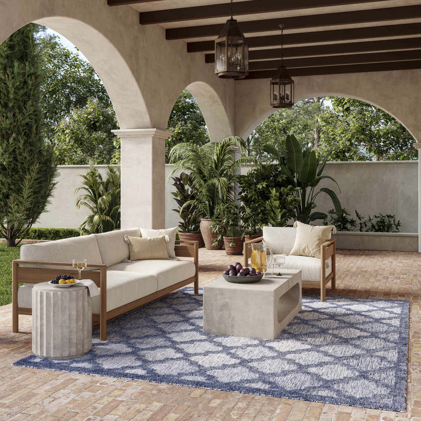 Outdoor patio with sofa, chair, and Nourison Easy Care Denim Blue Modern Area Rug with geometric pattern.