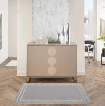 Hallway scene with a grey and ivory Nourison Essentials area rug, wood floors, and modern cabinet.