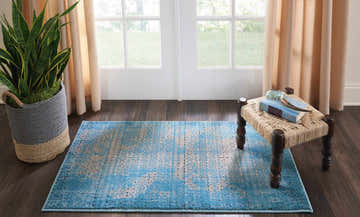 Light-filled room with a blue vintage Nourison Karma area rug, woven stool, and potted snake plant on dark wood floors.