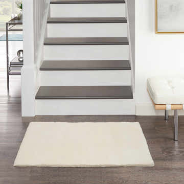 Entryway with white stairs and Nourison Plush Cloud Ivory rug on dark wood floor.