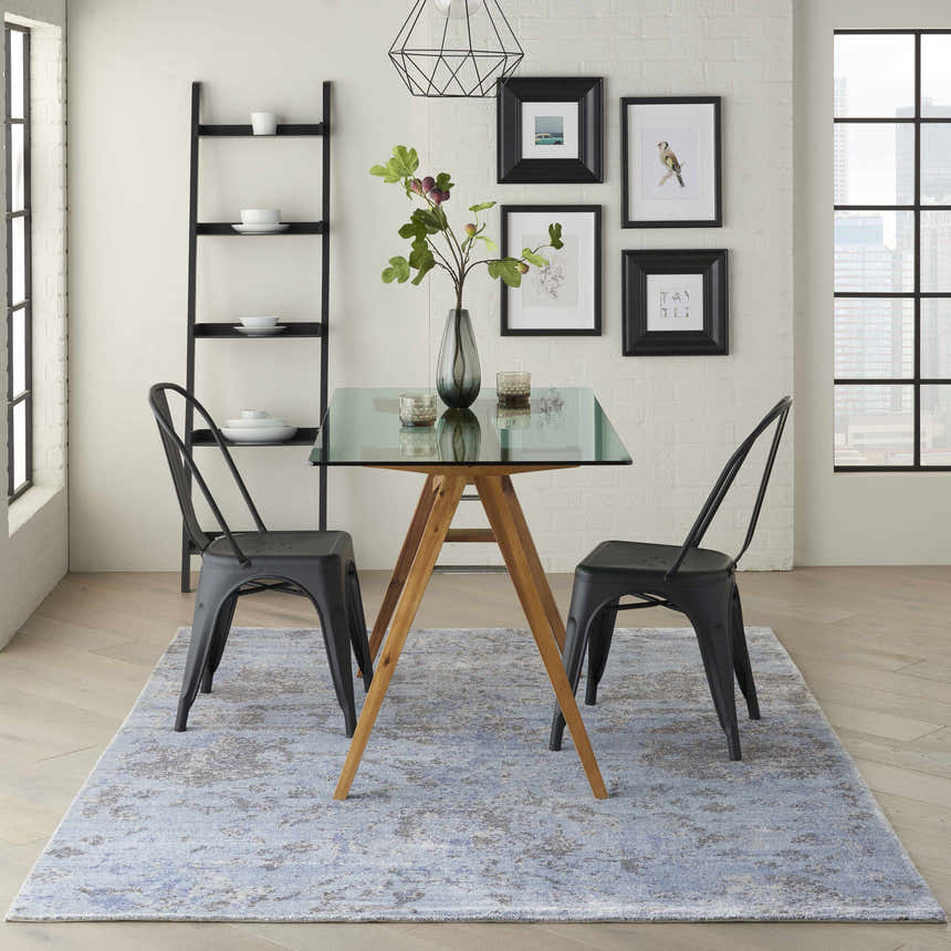 Modern dining room with sky blue Nourison Lucent Sky rug, glass-top table, and black metal chairs.