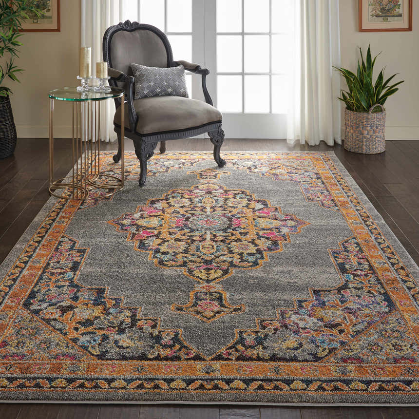 Living room scene with a Nourison Passionate Grey Bohemian Indoor Area Rug, gray chair, glass table, and dark wood floors.