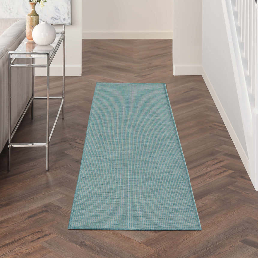 Hallway scene with a Nourison Positano Aqua rug, herringbone wood floors, and a modern glass console table.
