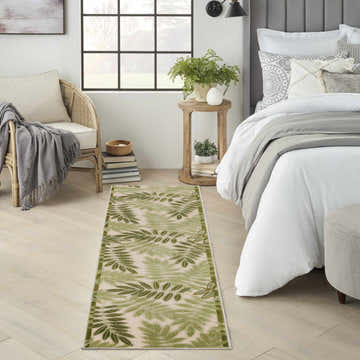 Bedroom scene with a Nourison Aloha Ivory Green Outdoor Area Rug runner, chair, bed, and side table.