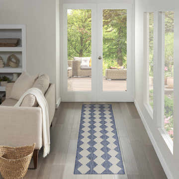 Hallway scene with a Nourison Positano Navy Blue runner rug, neutral sofa, and view of outdoor patio.