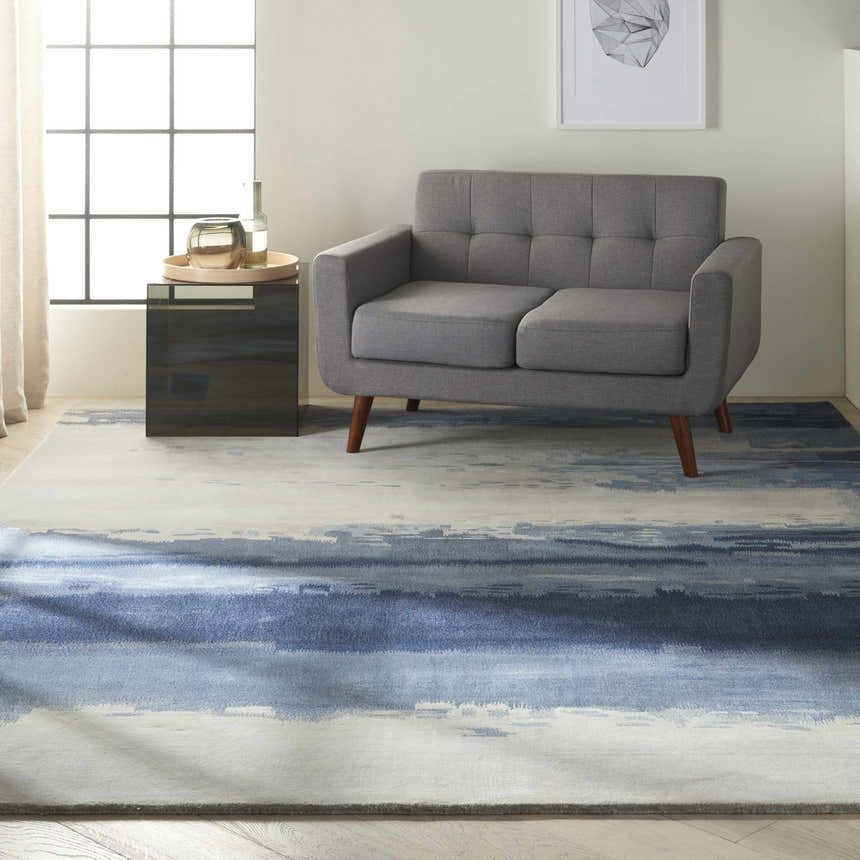 Living room scene with a gray sofa and blue Calvin Klein Home Luster Wash Shade rug. Modern, serene style.