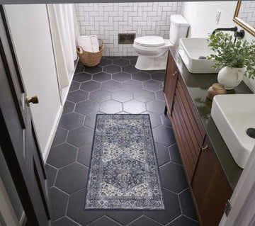 Bathroom scene with Nourison New Concept Navy Ivory Vintage Rug on black hexagon tile floor. Modern vanity, white walls.