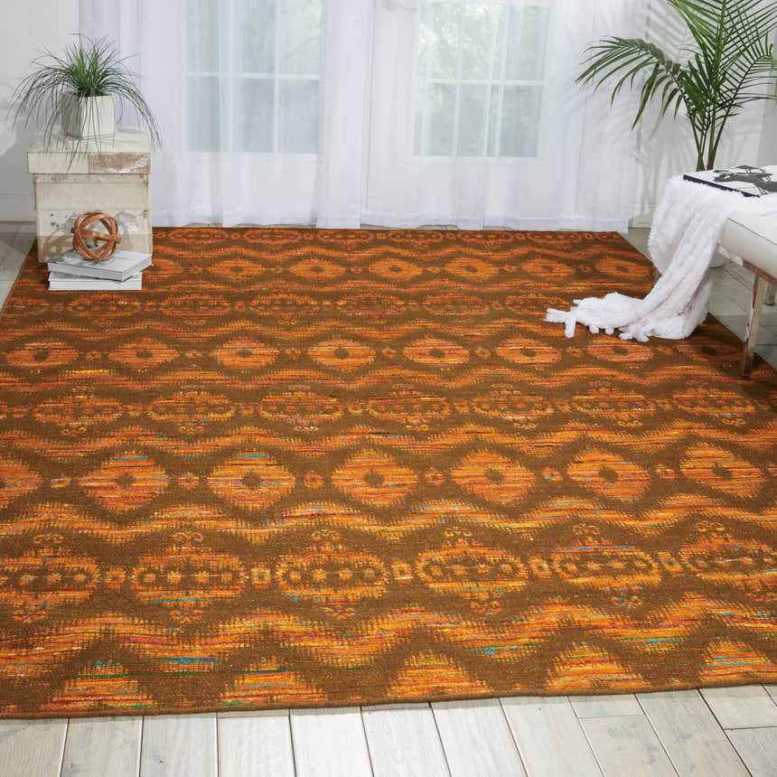 Living room scene with Nourison Spectrum Flame Chocolate rug, tribal pattern, white bench, and bright natural light.