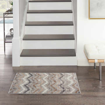 Entryway with stairs and a Nourison Elation Grey Ivory rug on dark wood floors. Modern bench and table.