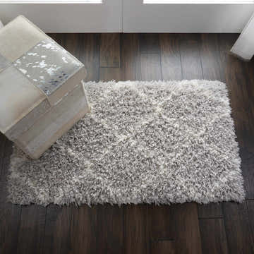 Entryway scene with Nourison Luxe Shag Grey Ivory rug on dark wood floor, paired with a neutral patchwork ottoman.