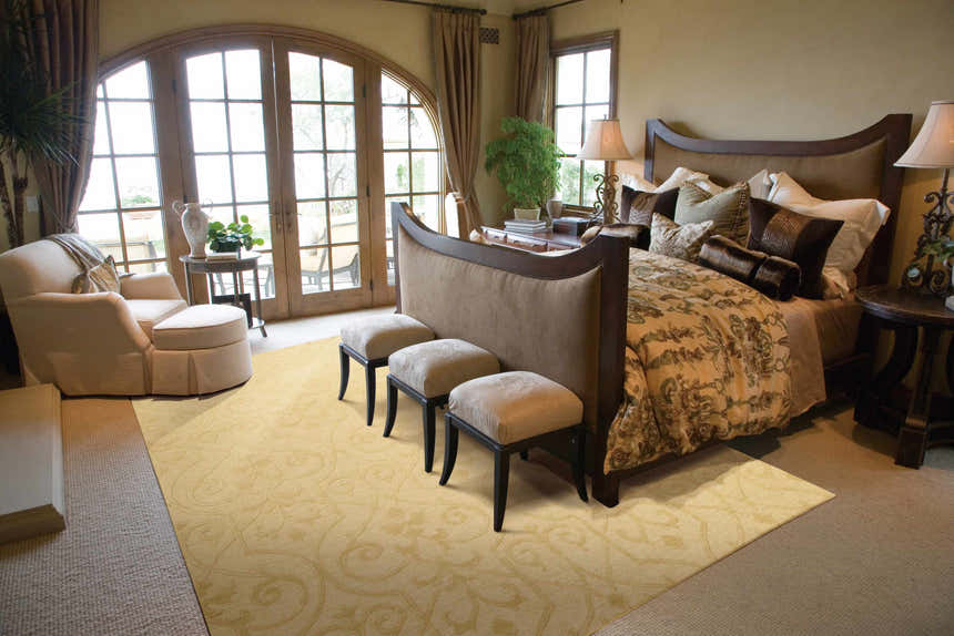 Tan bedroom scene with a Nourison Ambrose Straw Indoor Area Rug, upholstered bench, and French doors.