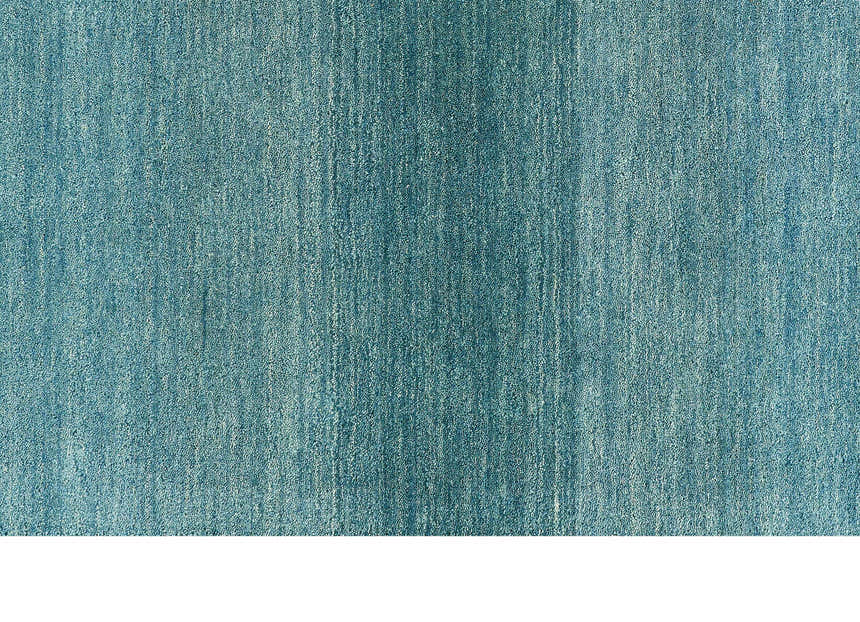 Close-up of the textured, aqua-colored Calvin Klein Linear Glow wool rug, a contemporary handmade design.