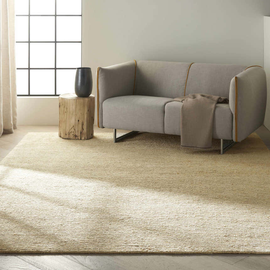 Living room scene with a Calvin Klein Mesa Gypsum rug, gray sofa, wood side table, and natural light.