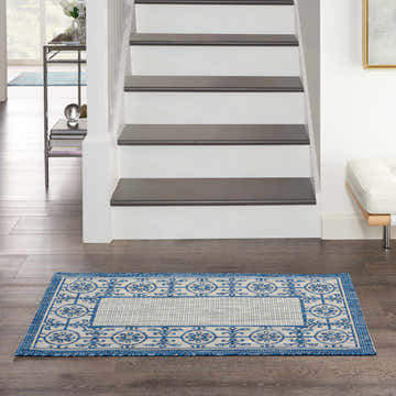 Entryway scene with Nourison Country Side Ivory Blue Transitional Area Rug on dark wood floors by stairs.
