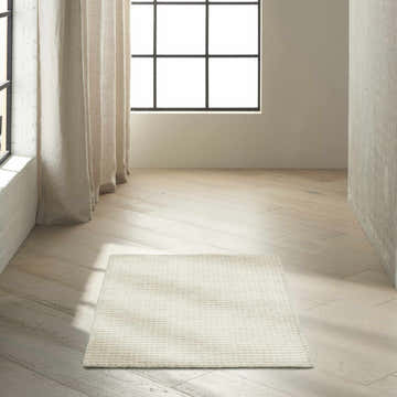 Minimalist room scene with ivory Calvin Klein Pretoria rug on light wood floor. Neutral tones, natural light.