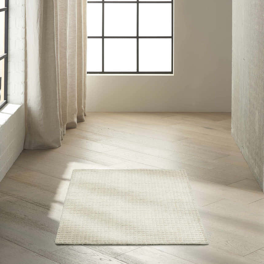 Minimalist room scene with ivory Calvin Klein Pretoria rug on light wood floor. Neutral tones, natural light.