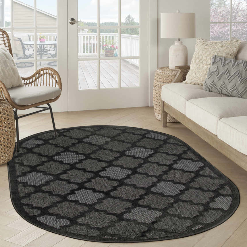 Living room scene with an oval Nourison Easy Care Charcoal Black rug, wicker chair, and neutral sofa.
