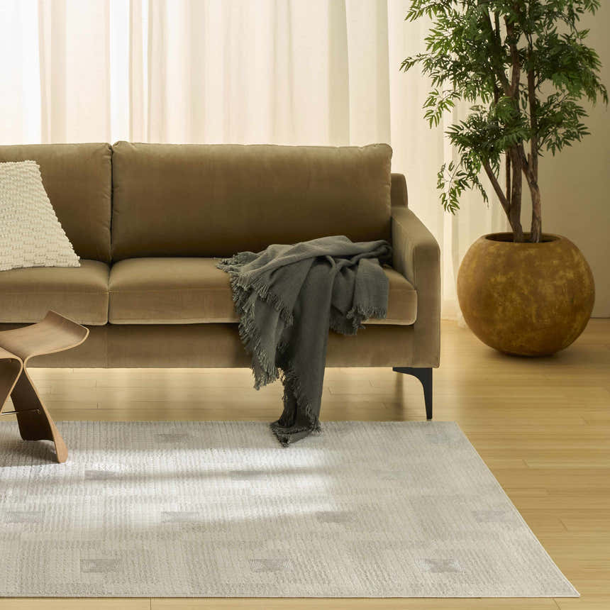 Living room scene with a Nourison Nordic Ivory Beige rug, chestnut sofa, wood floors, and potted tree.