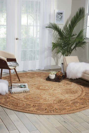 Light-filled room with a round Nourison 2000 Light Gold rug, chairs, and a potted palm for a relaxed, elegant feel.