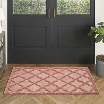 Entryway with a Nourison Easy Care Coral Orange Modern Area Rug, black door, and herringbone wood floor.