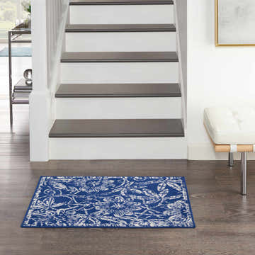 Entryway with a Nourison Whimsicle Navy Farmhouse Indoor Area Rug, white stairs, wood floors, and a modern white bench.