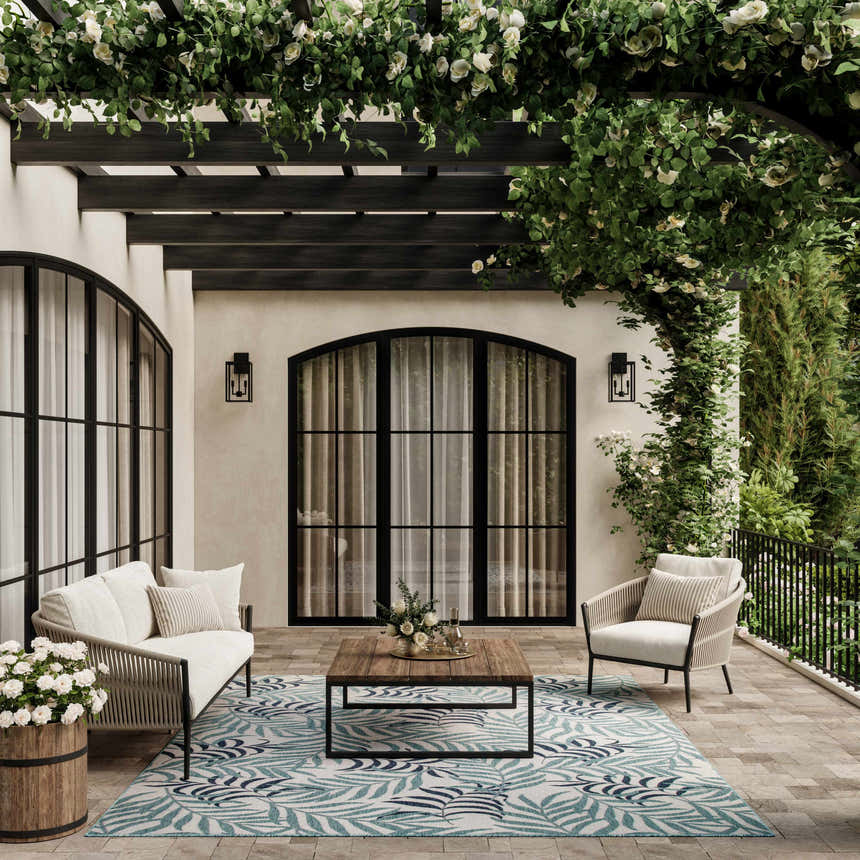 Outdoor patio with white furniture and Nourison Garden Oasis Blue Tropical Area Rug with palm leaf pattern.