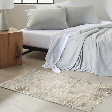 Bedroom scene with a Calvin Klein CK005 Enchanting Cream Grey rug, wood nightstand, and gray bedding. Modern style.