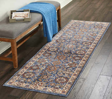 Hallway scene with a Nourison Lagos Blue Persian runner rug, gray bench, blue throw, and dark wood floors.