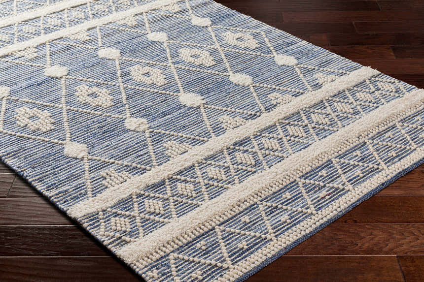 Close-up of the Eben Area Carpet. Hand woven cotton rug in light blue with an off-white geometric pattern. Corner