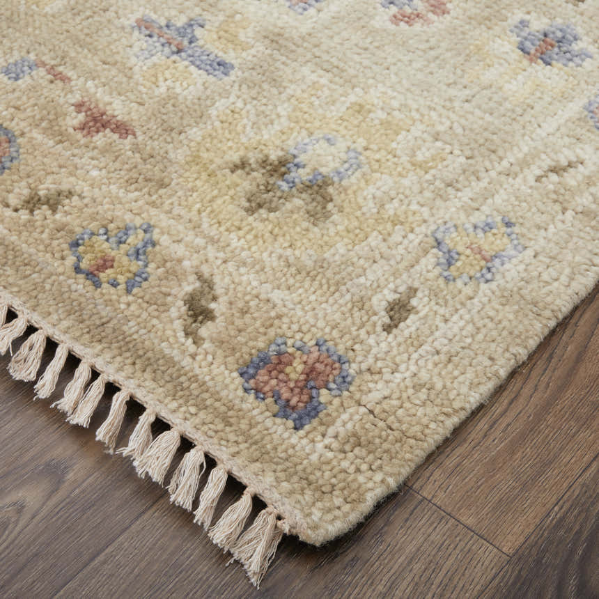 Close-up of the hand-knotted Feizy Fillmore rug. Tan wool rug with blue and dark red floral accents and fringe detail. Corner