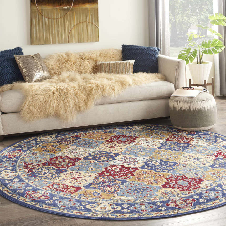 Bohemian living room with a Nourison Grafix Multicolor round area rug, cream sofa, and blue and gold pillows.