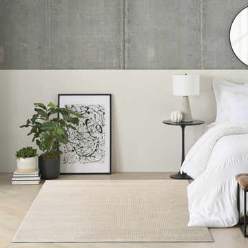 Bedroom scene with a beige DKNY Atlantic Avenue rug, white bedding, and modern decor.