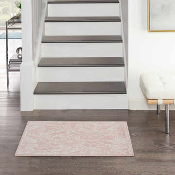Entryway scene with a Nourison Whimsicle Pink Farmhouse Indoor Area Rug on dark wood floors near stairs and a white bench.