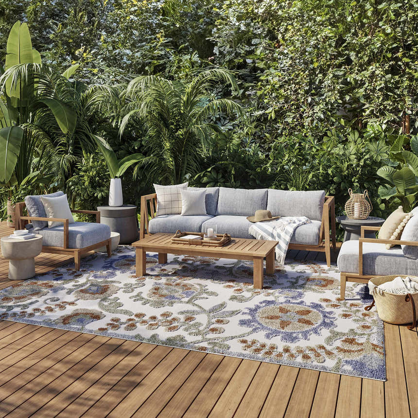 Outdoor patio scene with a Nourison Aloha Ivory Blue area rug, wood furniture, and lush greenery.