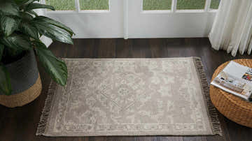 Entryway scene with a silver vintage Nourison Elan rug, dark wood floors, plant, and woven ottoman.