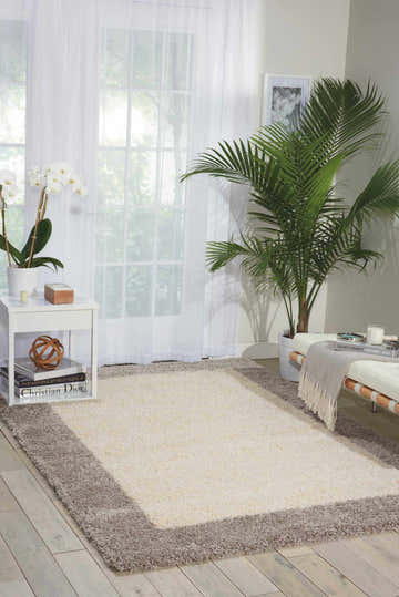 Living room scene with Nourison Amore Ivory Silver shag rug, white sofa, sheer curtains, and potted plants for a bright, airy look.