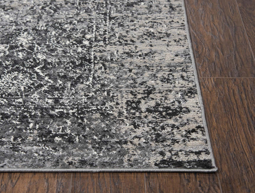 Close up of Rizzy EN7272 area rug showing abstract black, ivory, and gray pattern on dark wood floor. Corner