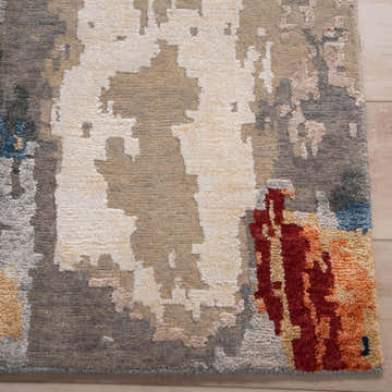 Close-up of Rizzy EVO443 area rug. Hand-knotted wool and tencel rug with beige, ivory, gray, blue, red, and orange abstract design. Corner