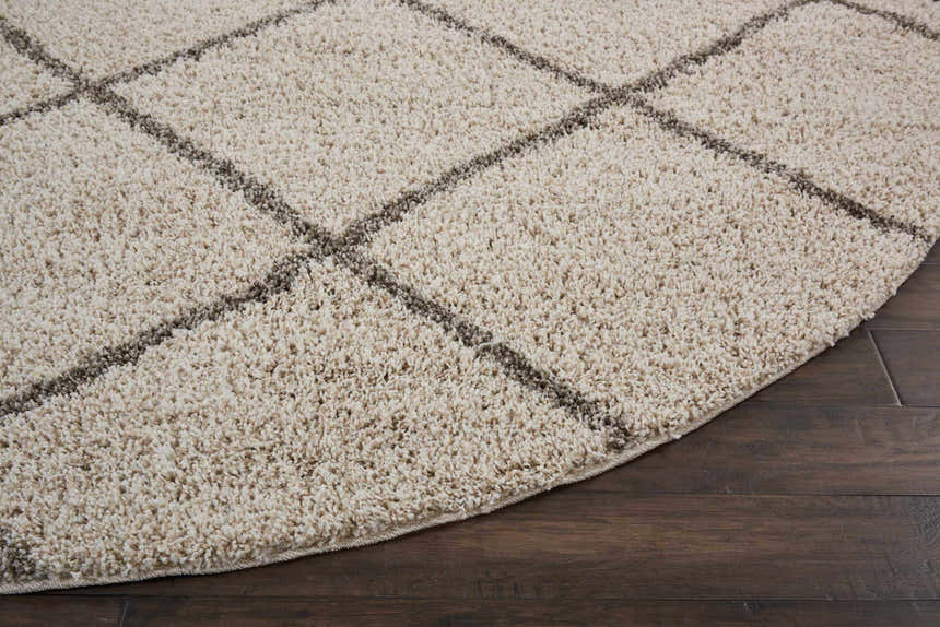 Close-up of a round Nourison Brisbane Cream Shag Rug showing its plush texture and geometric pattern on dark wood floors.