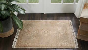 Entryway scene with a Nourison Elan Gold Vintage Area Rug. Dark wood floor, potted plant, and white door.