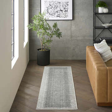 Modern living room scene with a DKNY Grand Street Light Grey runner rug on dark wood floors. Tan leather couch and abstract art.