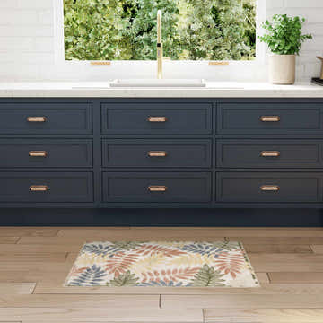 Kitchen scene with Nourison Aloha Ivory Rose rug, navy cabinets, light wood floors, white countertops, and gold faucet.